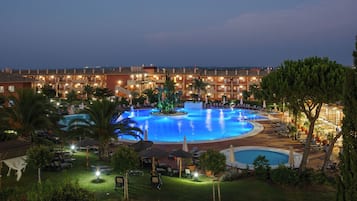Un hotel con una amplia piscina exterior, varias zonas de descanso y un jardín bien iluminado.