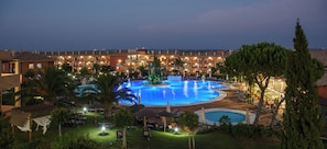 A hotel with a large outdoor swimming pool, multiple lounge areas, and a well-lit garden. - Ilunion Sancti Petri (Chiclana de la Frontera)
