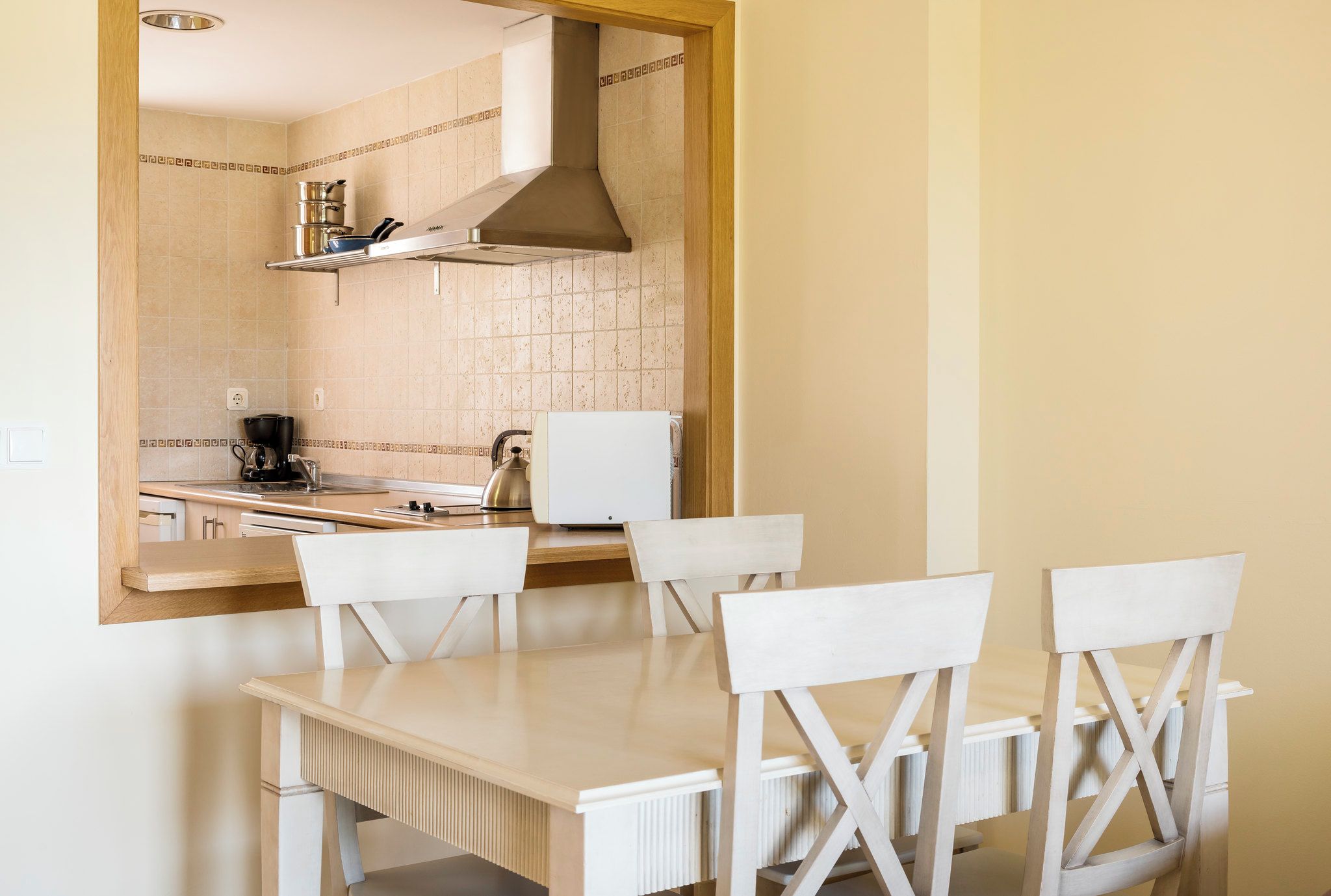 Cocina compacta con encimera blanca, estufa y microondas. Hay una silla de madera y una mesa blanca.