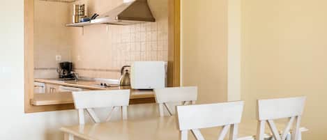 A compact kitchen with a white countertop, a stove, and a microwave. There is a wooden chair and a white table.