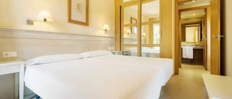 A hotel room with two beds, a bathroom with a mirror, and a small table.