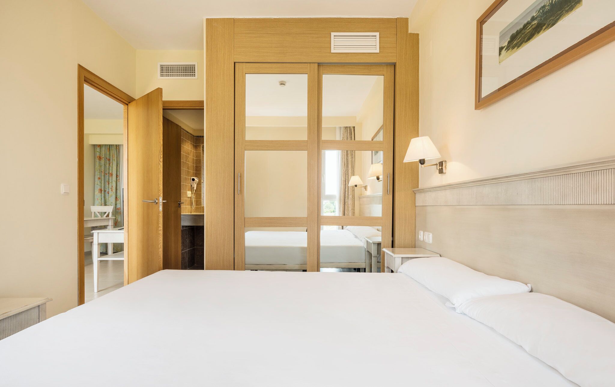 Habitación de hotel con una cama grande, un armario de madera, un baño con ducha y una mesita con lámpara.