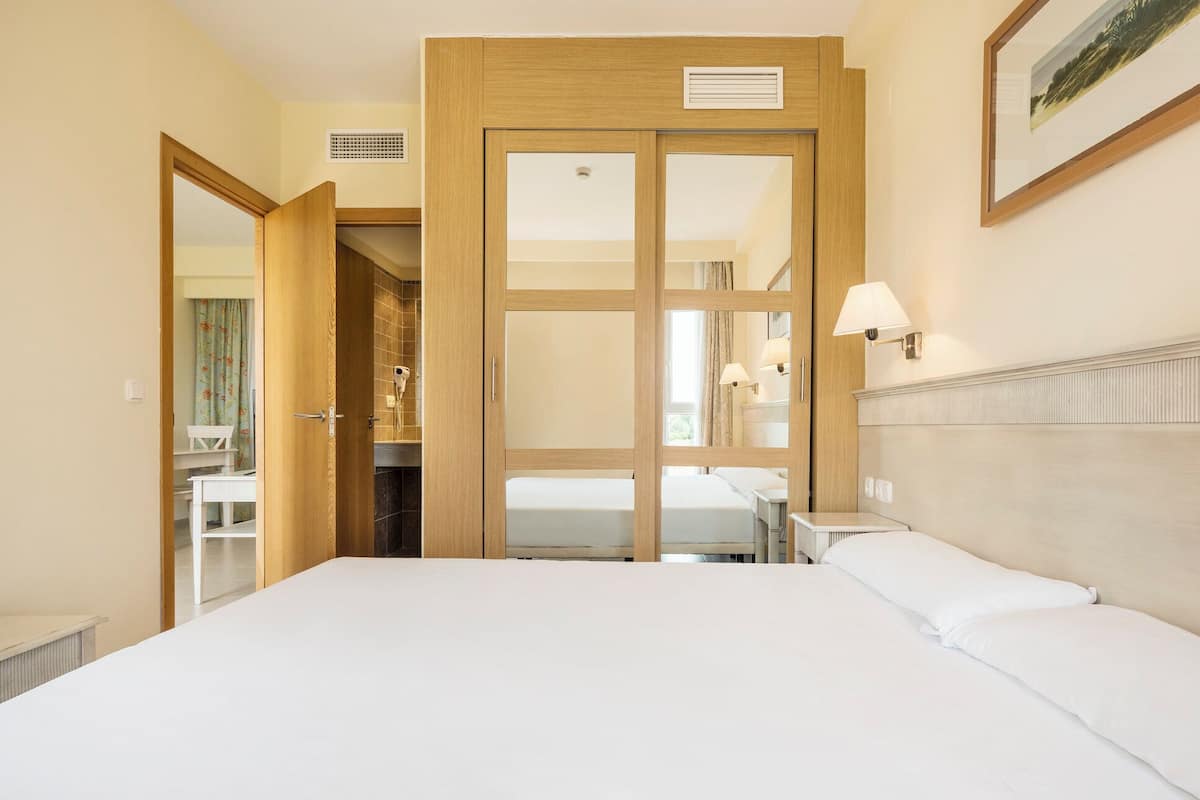 Habitación de hotel con una cama grande, un armario de madera, un baño con ducha y una mesita con lámpara.