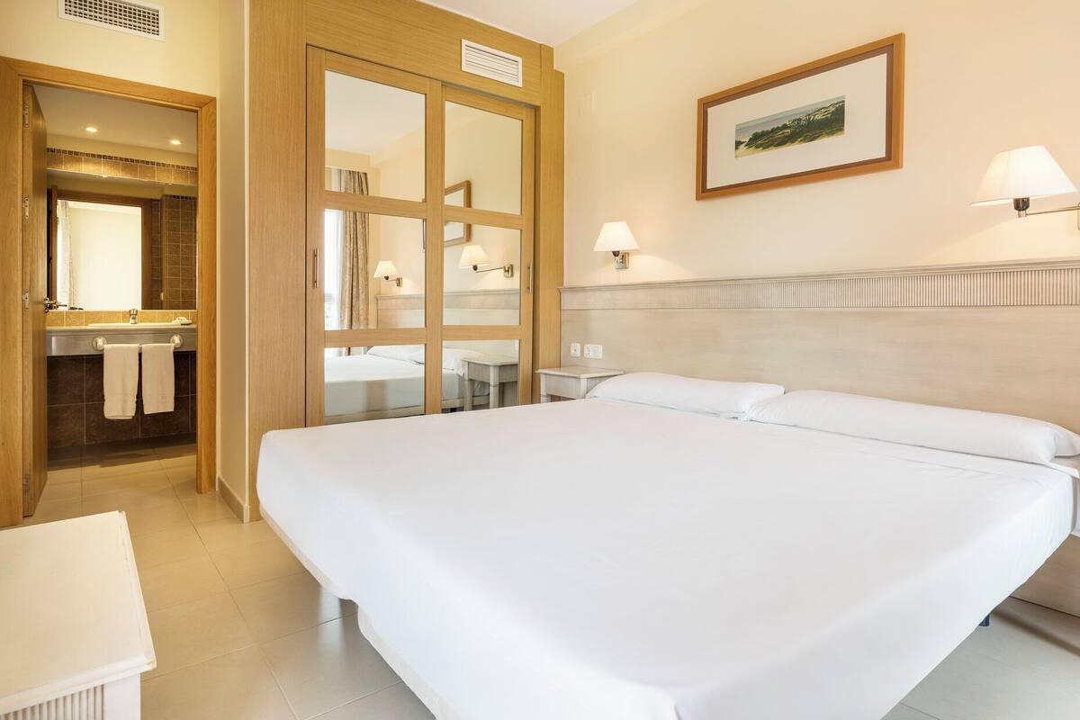 A hotel room with a large bed, a bathroom with a mirror and sink, and a painting on the wall.