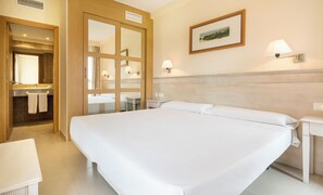 A hotel room with a large bed, a bathroom with a mirror and sink, and a painting on the wall. - Ilunion Sancti Petri (Chiclana de la Frontera)