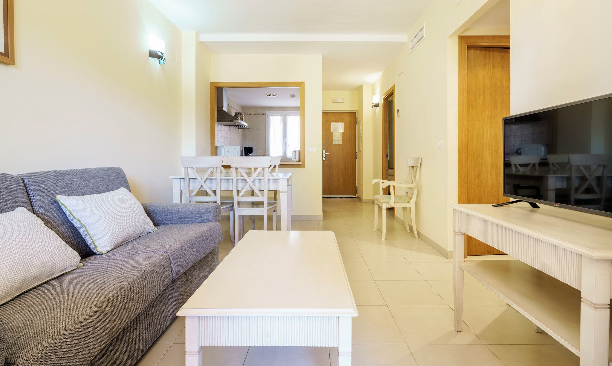 Una sala de estar con un sofá gris, una mesa de centro blanca y un televisor sobre un mueble.