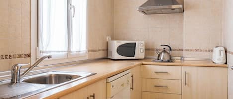 A kitchen with a stainless steel sink, a microwave, a kettle, and wooden cabinets.