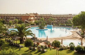 Un complexe hôtelier doté d’une grande piscine centrale, de plusieurs piscines plus petites et d’un vaste espace pelouse bien entretenu, agrémenté de chaises longues et de parasols.