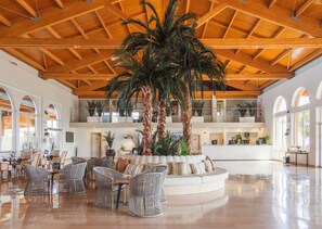 A spacious lobby with high ceilings, a central palm tree, and multiple seating areas. - Ilunion Sancti Petri (Chiclana de la Frontera)