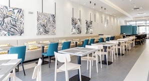 A modern dining area with long tables, blue and white chairs, and abstract art on the walls. - Ilunion Sancti Petri (Chiclana de la Frontera)