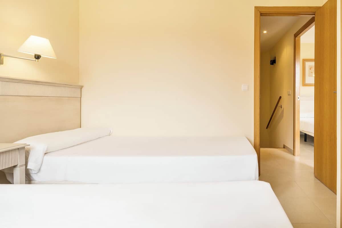 Una habitación de hotel con dos camas, una mesita de noche, una lámpara y una puerta de madera.