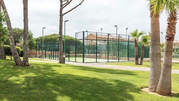 Una cancha de tenis rodeada por una valla verde, árboles y un banco.