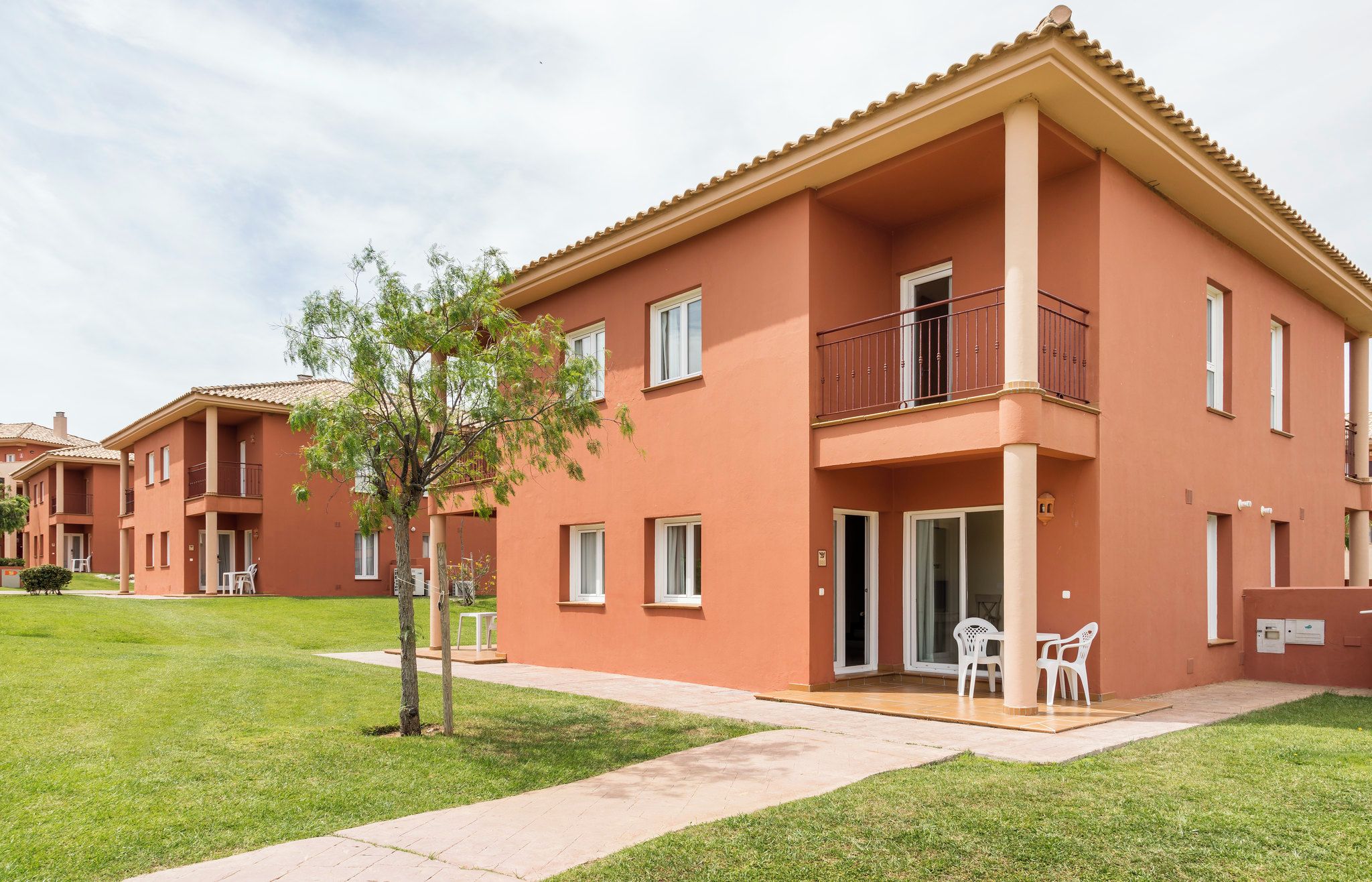 Un edificio residencial de varios pisos con techo plano, balcones y un pequeño patio con mobiliario exterior.