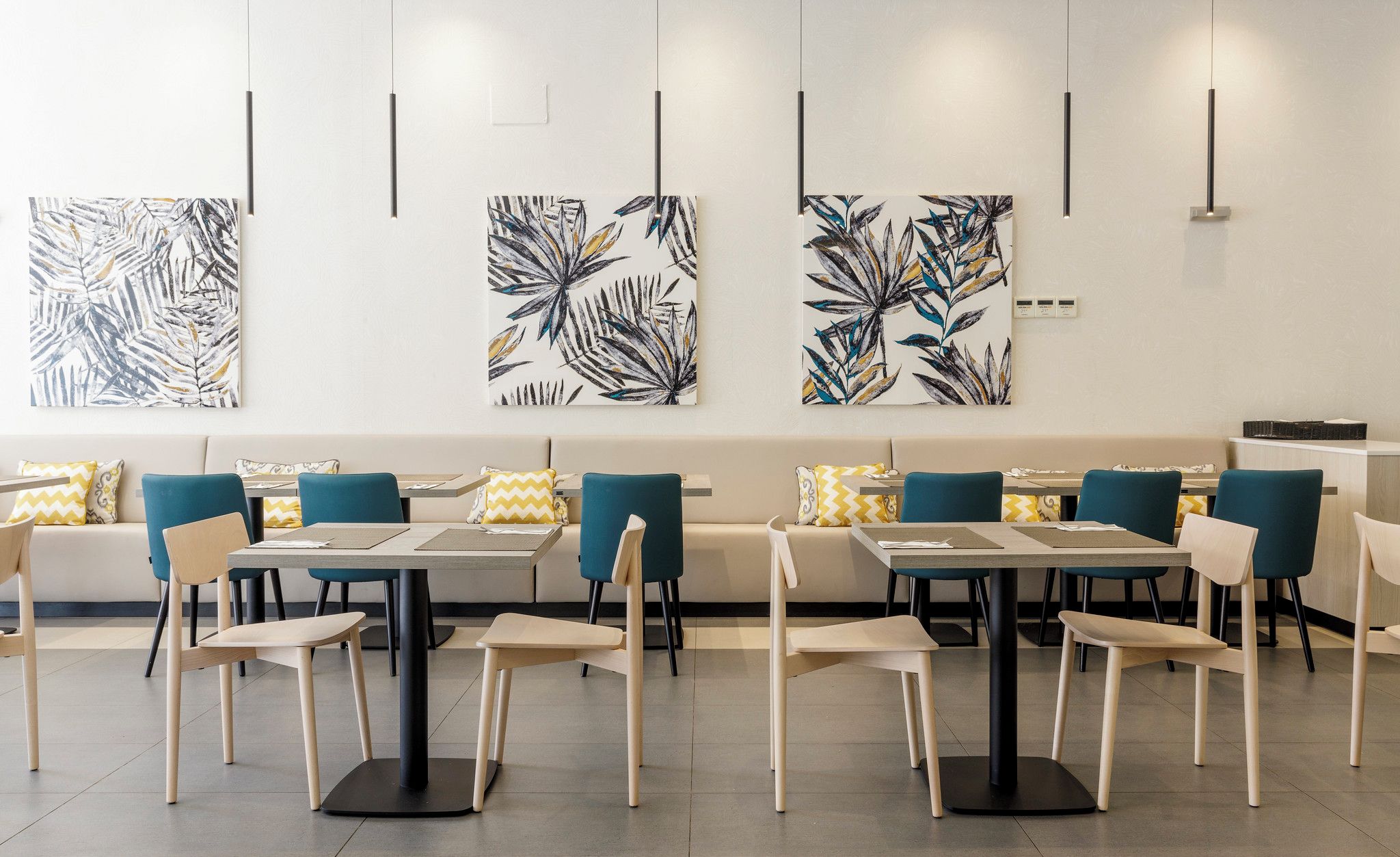 Un comedor moderno con mesas, sillas, un sofá y arte mural abstracto con estampado de hojas.