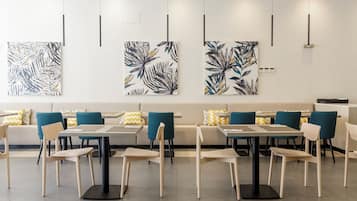 Un comedor moderno con mesas, sillas, un sofá y arte mural abstracto con estampado de hojas.