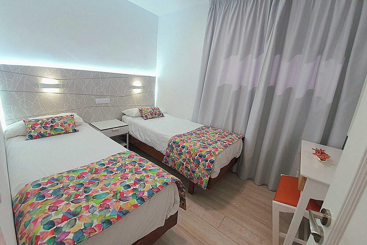Quarto de hotel com duas camas, uma pequena escrivaninha e uma cadeira.