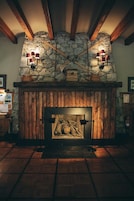 Una chimenea de piedra con repisa de madera, dos apliques de pared y un cuadro enmarcado encima.