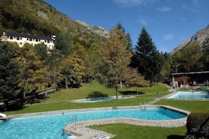 Un área de piscina con varias piscinas, rodeada de árboles y un paisaje montañoso.