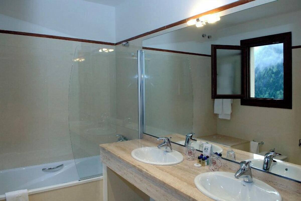 Une salle de bain dotée de deux lavabos, d’une douche en verre et d’un grand miroir offrant une vue sur un paysage montagneux.