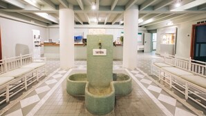 Un espace d’accueil doté d’un sol carrelé, de bancs blancs et d’un pilier central portant l’inscription « TARTERA ».