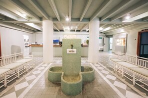 Un espace d’accueil doté d’un sol carrelé, de bancs blancs et d’un pilier central portant l’inscription « TARTERA ».
