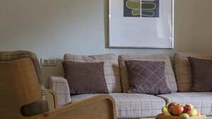 Un salon moderne avec un fauteuil en bois, un canapé agrémenté de coussins à carreaux et une œuvre d’art encadrée accrochée au mur.
