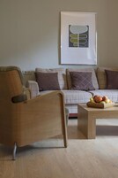 Una sala de estar moderna con un sillón de madera, un sofá con cojines escoceses y una obra de arte enmarcada en la pared.