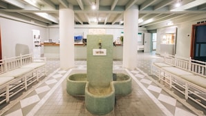 Un espace d’accueil doté d’un sol carrelé, de bancs blancs et d’un pilier central portant l’inscription « TARTERA ».