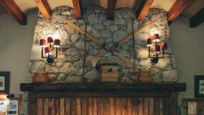 Une cheminée en pierre avec un manteau en bois, deux appliques murales et un tableau encadré au-dessus.