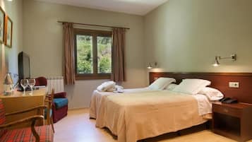 Une chambre d’hôtel avec deux lits, une table de chevet en bois, un bureau avec une chaise, une fenêtre avec des rideaux et une vue sur la verdure.