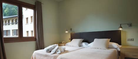 A hotel room with two beds, a nightstand, a lamp, and a window with curtains.