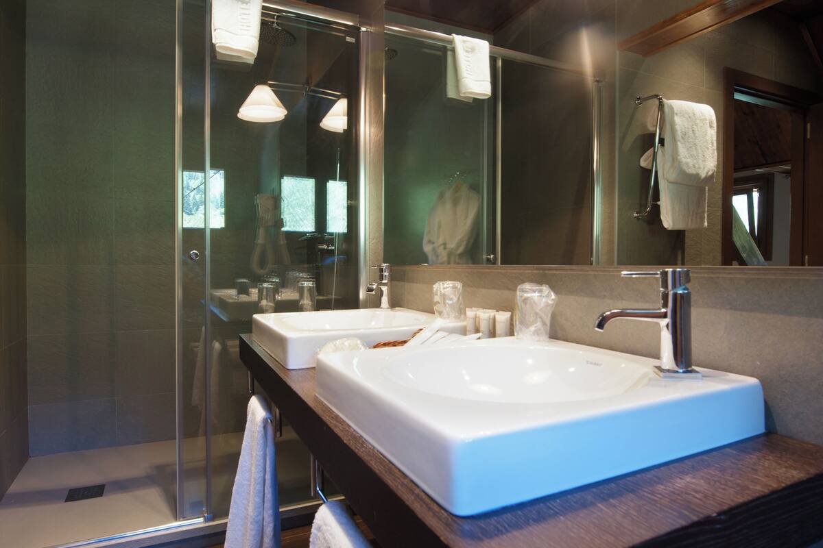 Une salle de bain moderne avec deux vasques, une douche à l’italienne en verre et un grand miroir.