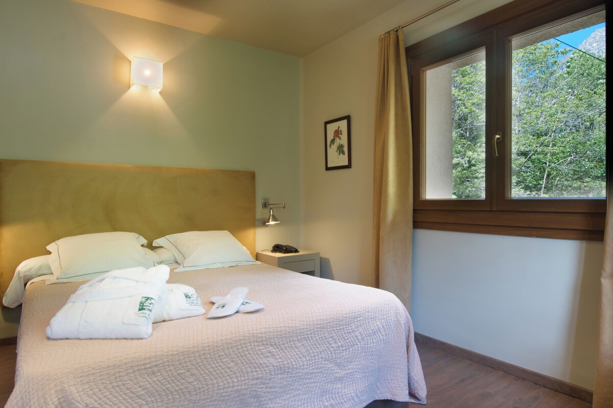 Ein Hotelzimmer mit Bett, Nachttisch, Lampe und einem Fenster mit Vorhängen.