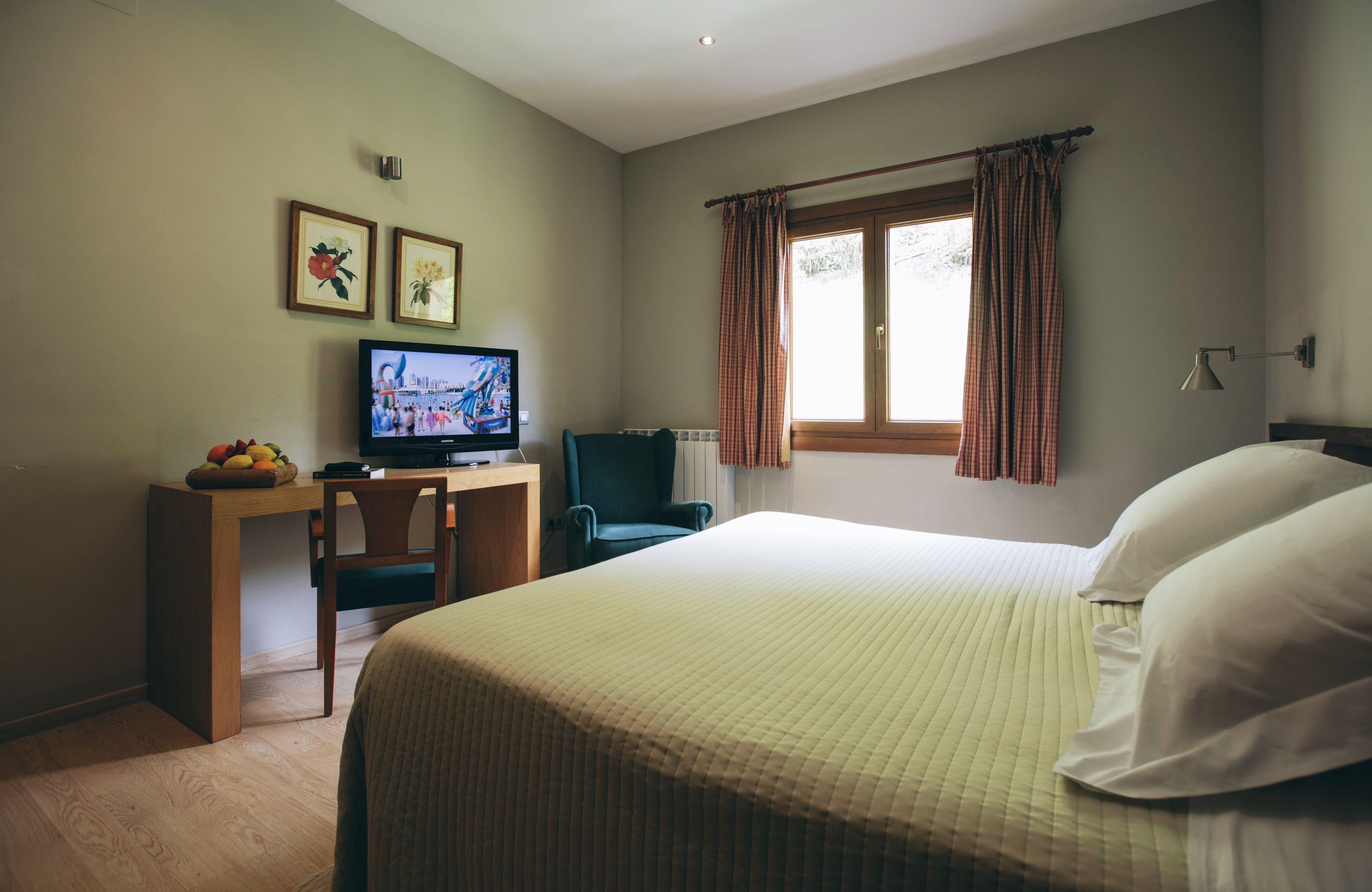 Una habitación de hotel con cama, escritorio, televisor, una silla y ventana con cortinas.
