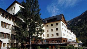 Un hôtel à plusieurs étages, de style architectural traditionnel, doté de balcons et offrant une vue sur les montagnes.