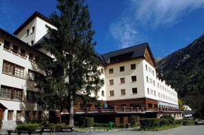 Un hôtel à plusieurs étages, de style architectural traditionnel, doté de balcons et offrant une vue sur les montagnes.