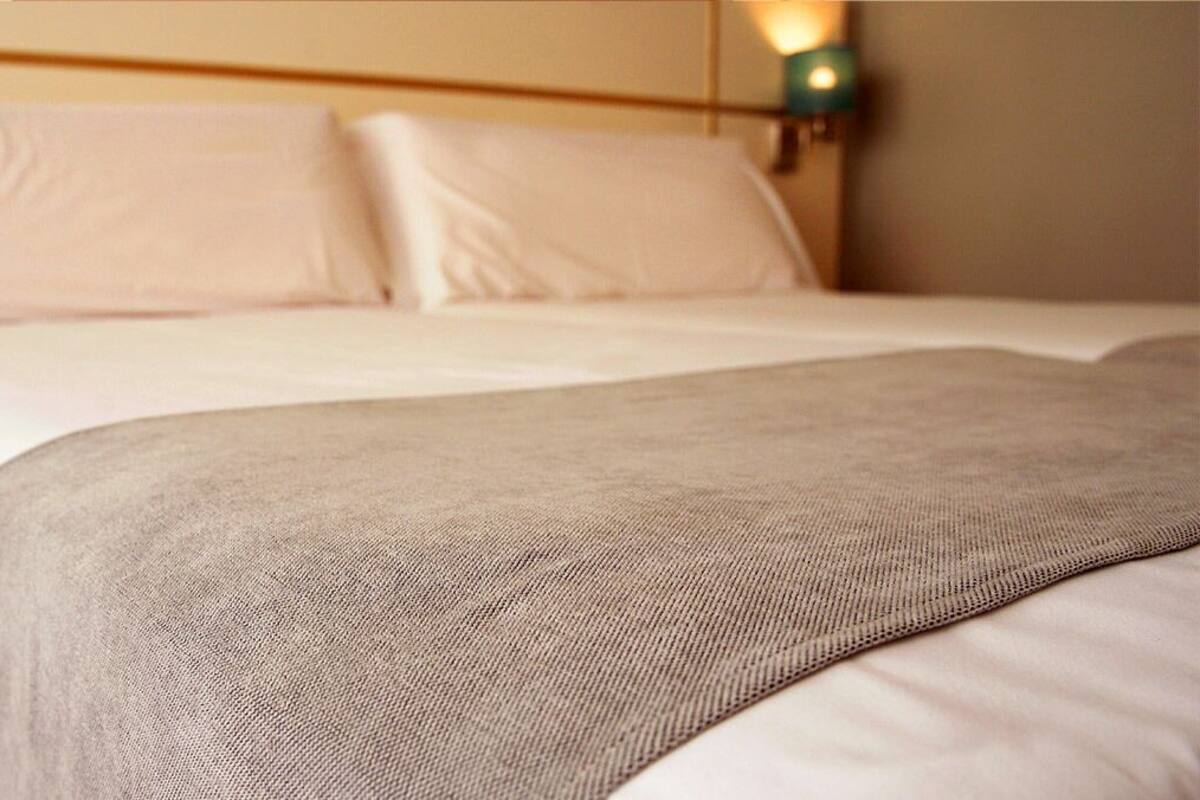 A neatly made bed with white linens and a beige throw blanket.