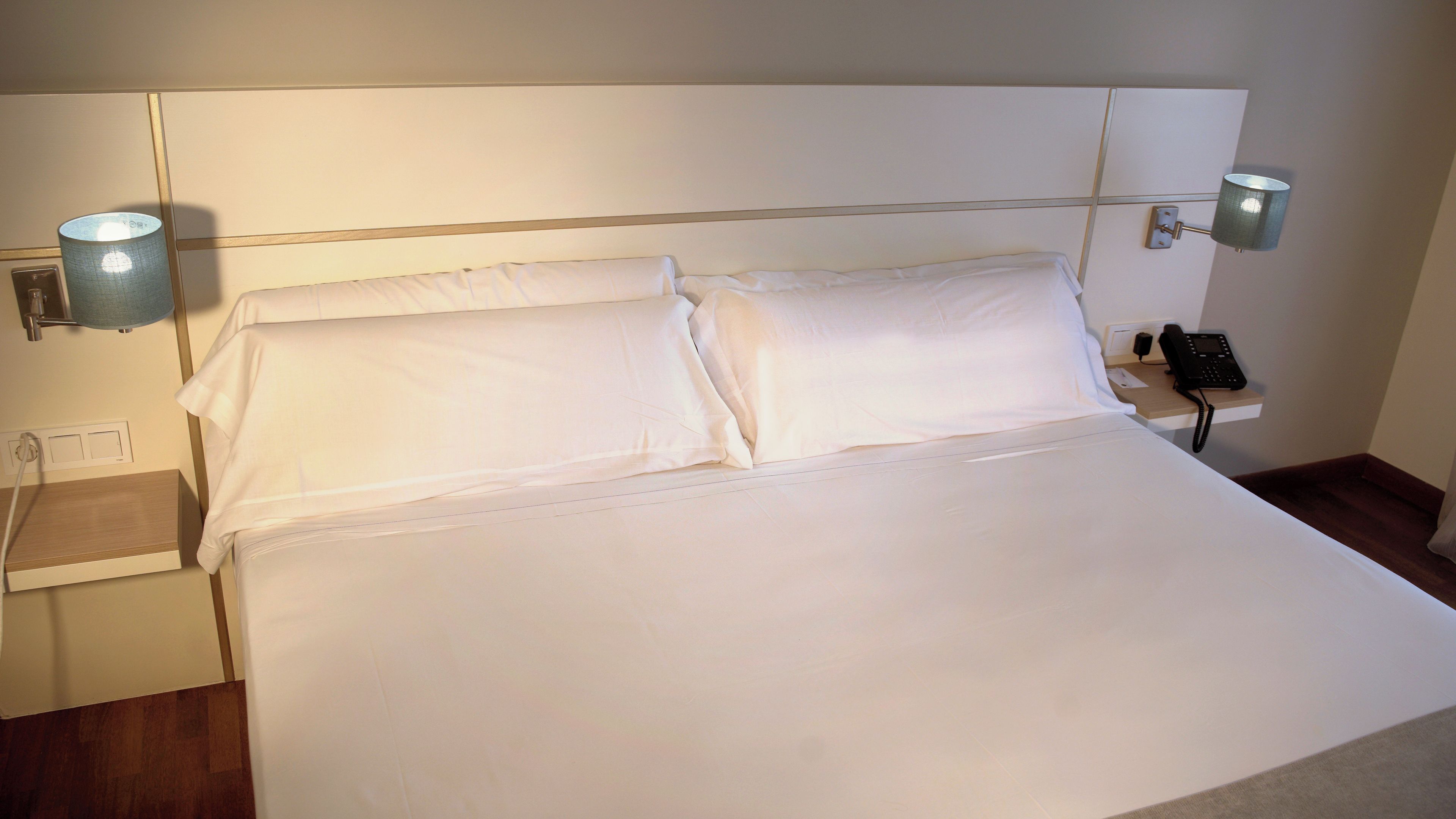 A hotel room with a large bed, two bedside lamps, a bedside phone, and a wooden nightstand.