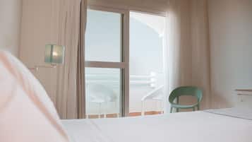 A hotel room with a bed, a chair, and a view of the sea through a sliding door.