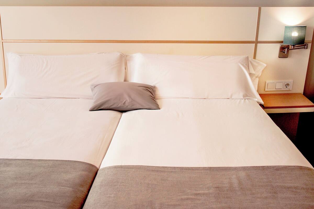 A double bed with two pillows, a bedside table with a lamp, and a wall-mounted light fixture.