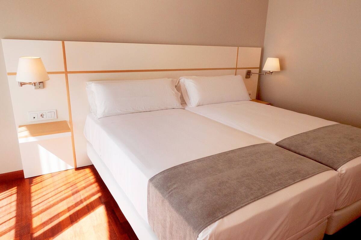 A double bed with a wooden headboard, two bedside lamps, and a bedside table with a lamp.