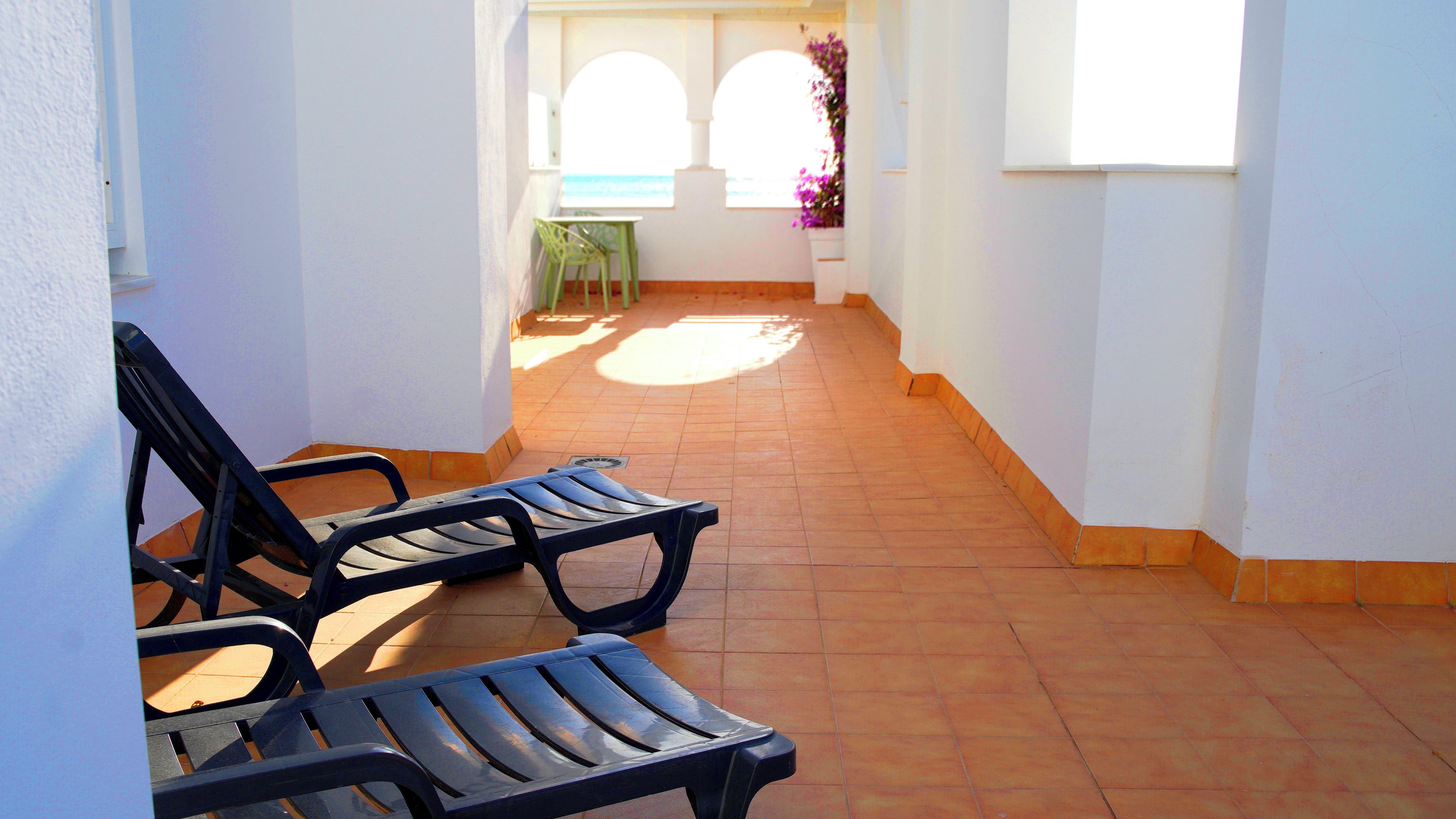 A corridor with two black metal chairs, a green chair, and a white table with a purple flower arrangement.