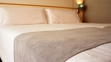A neatly made bed with white linens and a beige throw blanket.