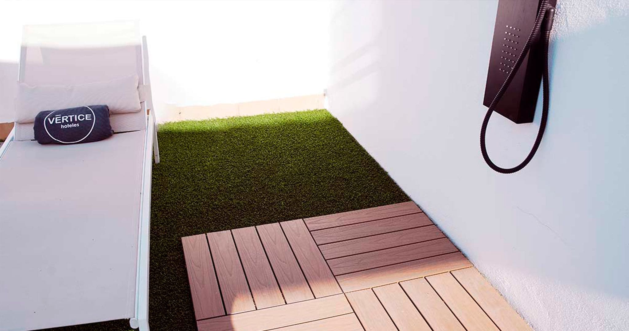 A room with a white bed, a black bag labeled "VERTICE", and a small wooden deck area.