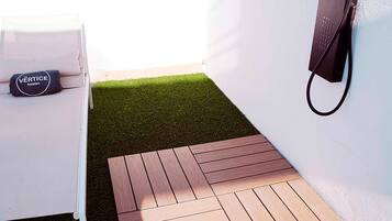 A room with a white bed, a black bag labeled "VERTICE", and a small wooden deck area.