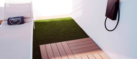 A room with a white bed, a black bag labeled "VERTICE", and a small wooden deck area.