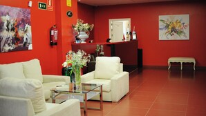 A lobby with red walls, a reception desk, white sofas, a glass coffee table, and a vase with flowers. - Hotel Vertice Chipiona Mar (Chipiona)