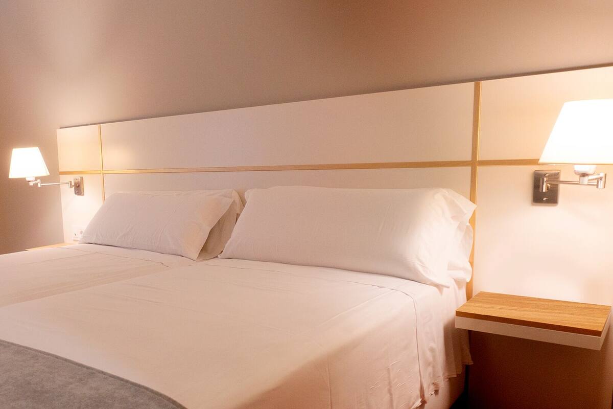 A hotel room with a large bed, two bedside lamps, and a wooden nightstand.