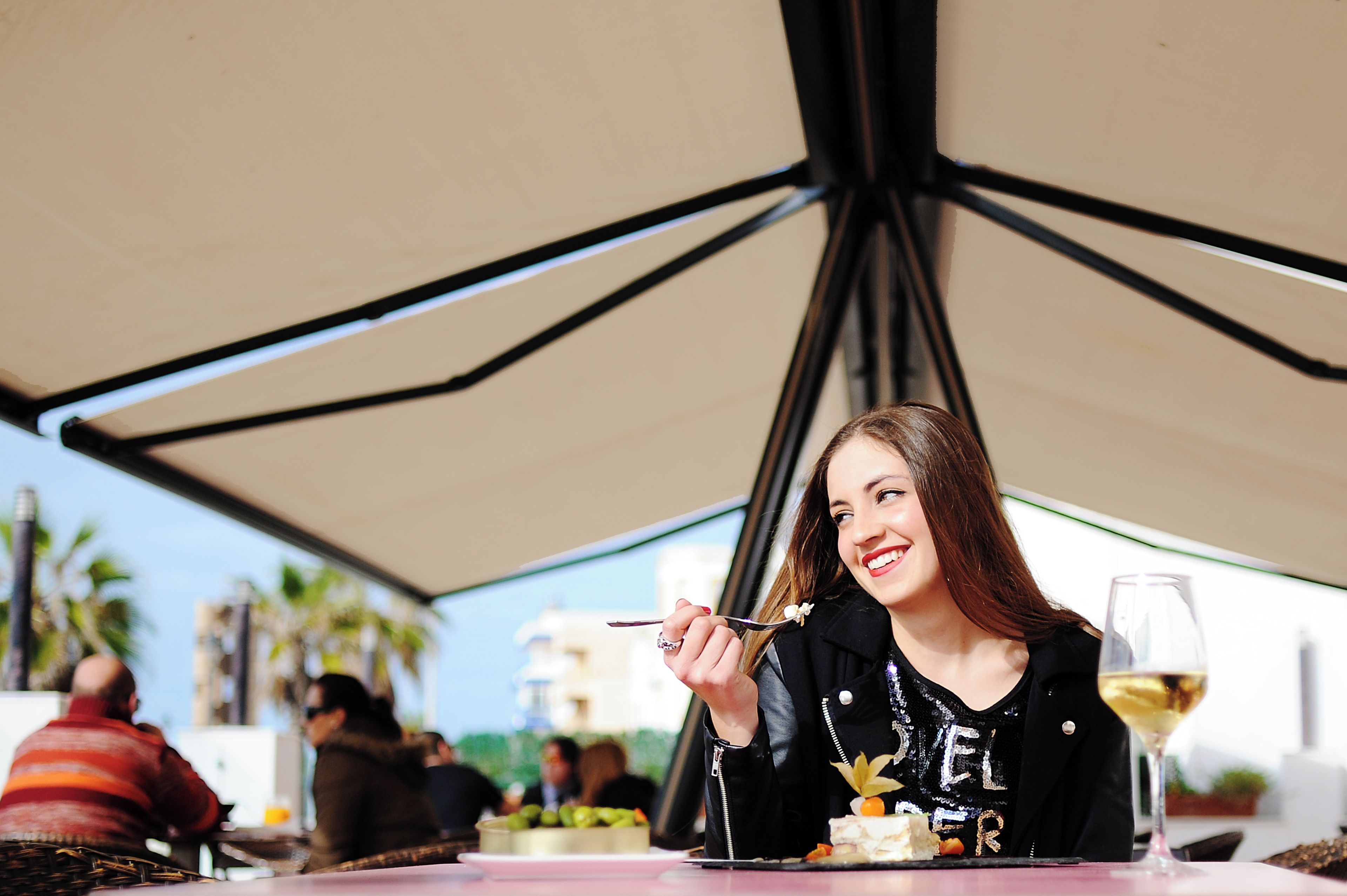 Una mujer cenando en una mesa al aire libre, con una copa de vino y un plato de postre.
