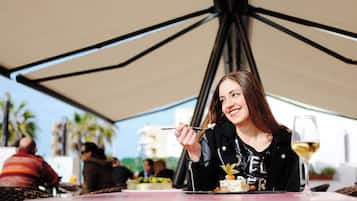 Una mujer cenando en una mesa al aire libre, con una copa de vino y un plato de postre.